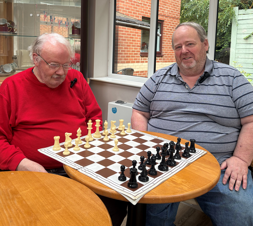 Ian and Stephen sitting behind chess board smiling.